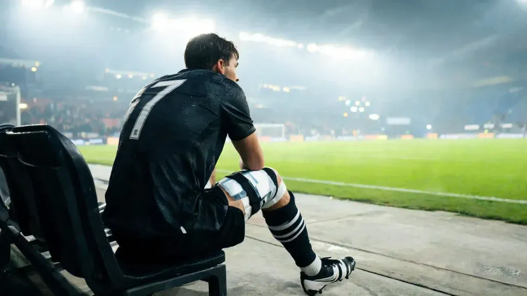 Jugador profesional en el banquillo tras un partido de alta exigencia física en el fútbol europeo.