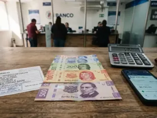 Billetes de pesos mexicanos y ficha de depósito bancario sobre un escritorio de trabajo.