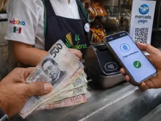 Mano sosteniendo billetes de pesos mexicanos junto a un teléfono inteligente realizando un pago digital.