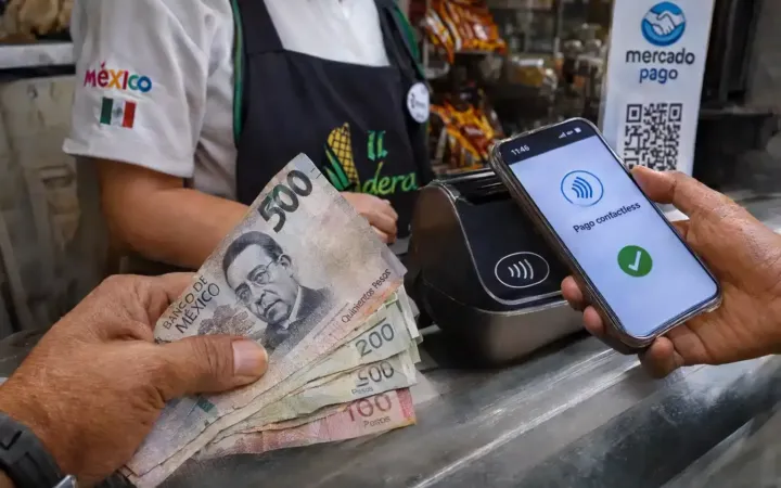 Mano sosteniendo billetes de pesos mexicanos junto a un teléfono inteligente realizando un pago digital.